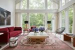 Modern living room with red sofa, red floral rug, coffee table, and large windows.