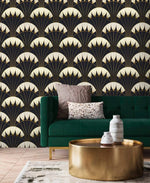 Art Deco black gold wallpaper behind green velvet sofa and gold round coffee table, repeating cream fan scallop pattern