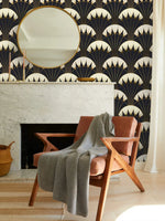 Art Deco black gold wallpaper above marble fireplace with round gold mirror, leather chair and grey throw in cozy room setting