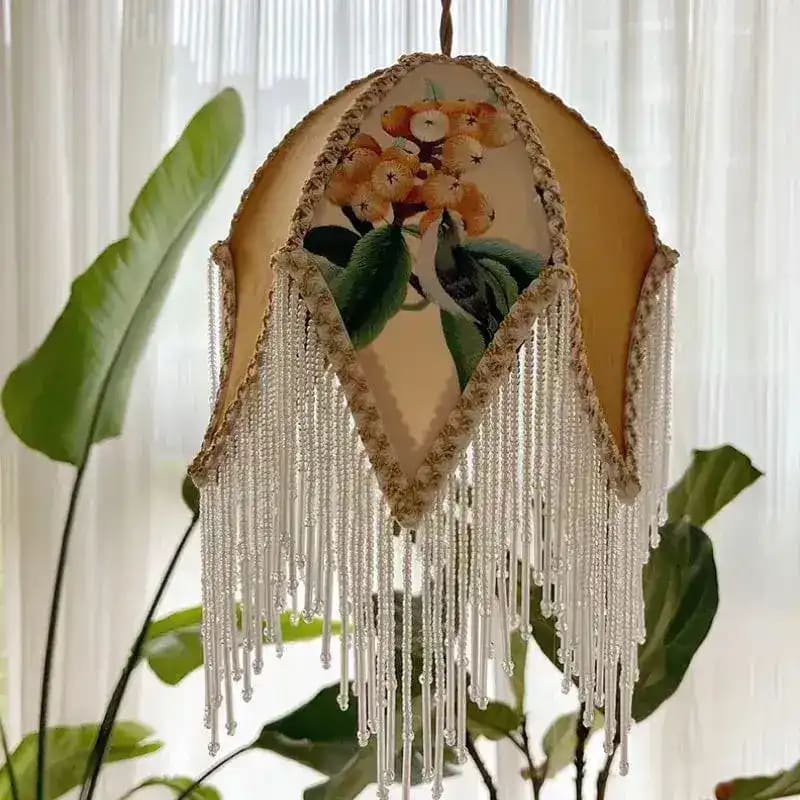 Asian jacquard lamp shade hanging with white beaded fringe, floral embroidery, backlit by sheer curtains with plants