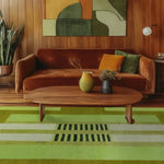 Stylish living room featuring a large green area rug with abstract design, perfect as an office wool rug. The space includes a wooden coffee table and a rust-colored sofa, creating a cozy atmosphere ideal for office settings.