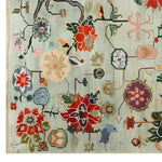 A vibrant Avant Bloom Knotted Wool Area Rug featuring an intricate array of colorful floral patterns and abstract designs on a light background. The rug showcases red, blue, and green hues in a harmonious blend, adding a touch of elegance and artistic flair to any room.