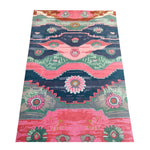 Colorful hand-tufted rug featuring Aztec geometric designs and floral medallions in shades of pink, teal, green, and dark blue.