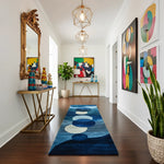 Modern hallway with a blue circular rug, gold console table, and colorful abstract art.