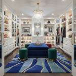 Luxurious walk-in closet with white shelves, blue ottoman, an abstract blue wool rug, and decorative items.