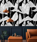 Banana leaf wallpaper panel above dark navy wall with copper pendant lights and tan leather armchair in a moody room