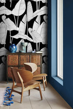 Banana leaf wallpaper behind a vintage carved cabinet with blue vases, paired with a sculptural wood lounge chair