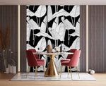 Oversized banana leaf wallpaper with white line-art leaves on black, installed behind dining table with pink chairs