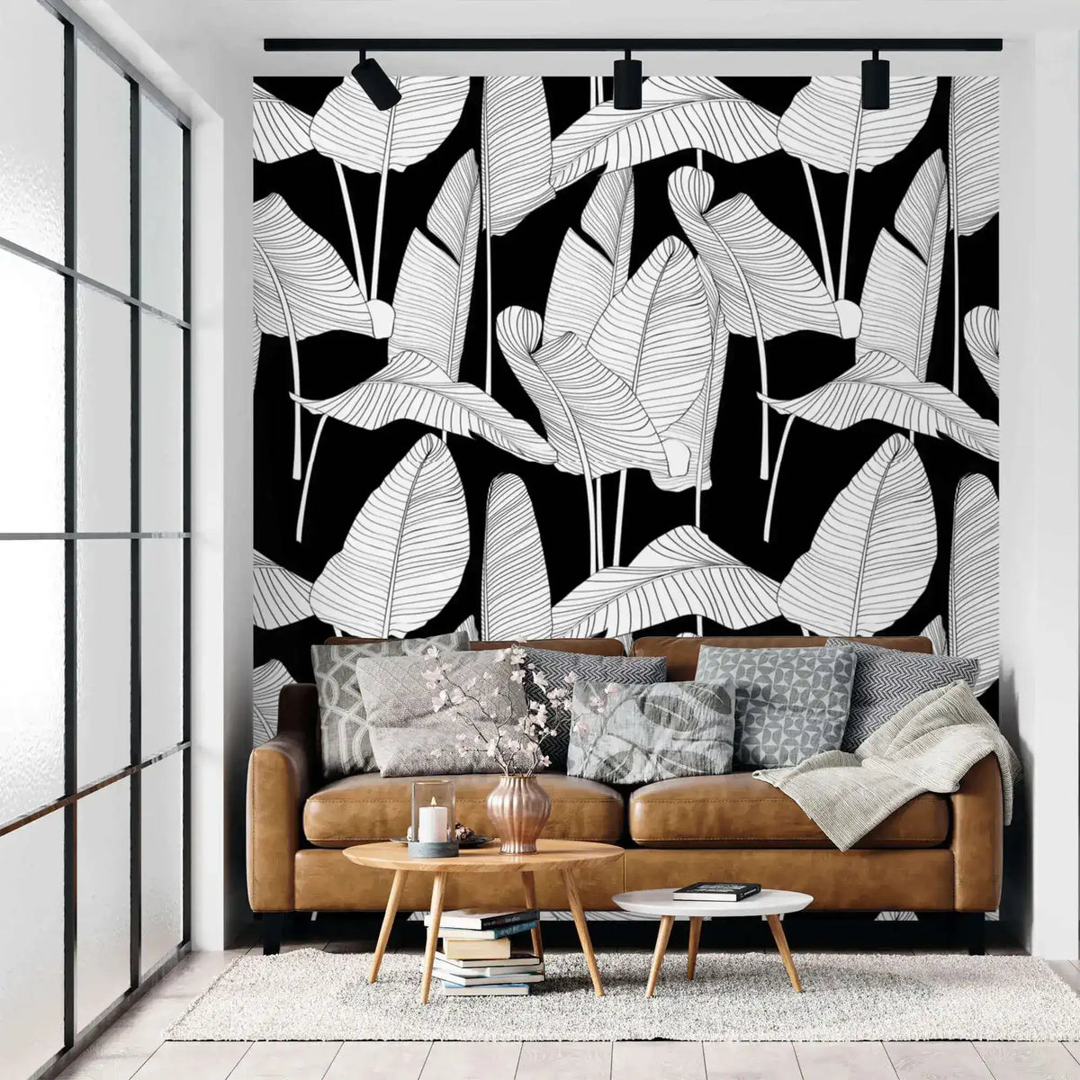 Banana leaf wallpaper with white line-art leaves on black behind a tan leather sofa in a modern living room