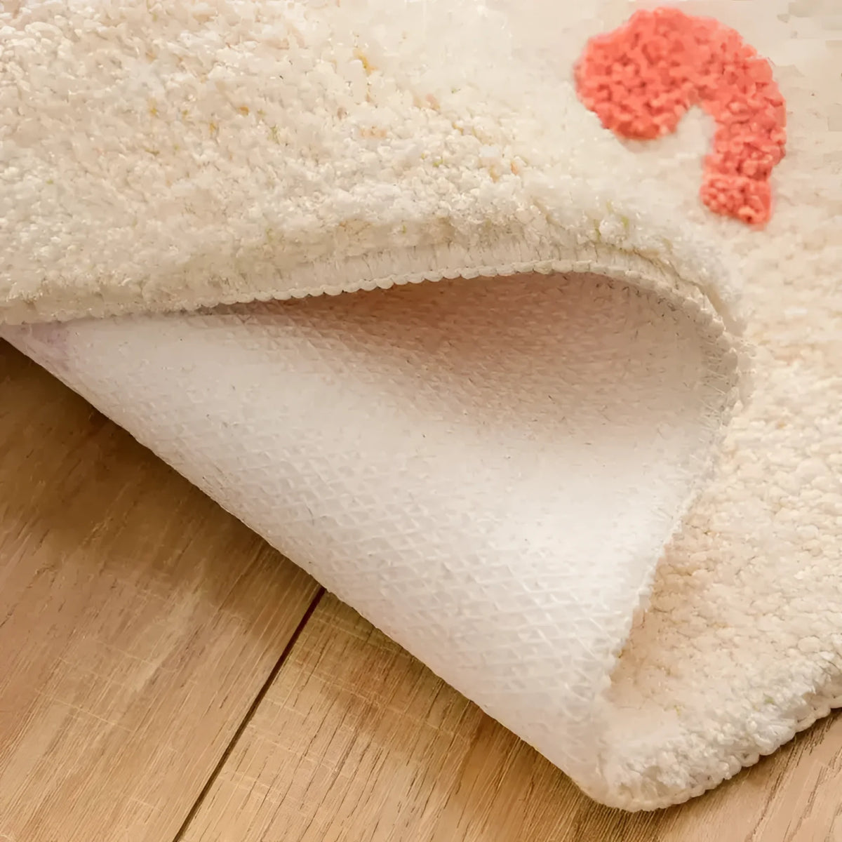 Close-up view of the Bebe Bathroom Mat showcasing its textured underside and soft, plush top layer. The mat is laid on a wooden floor, highlighting its cozy and absorbent material, ideal for any bathroom decor.