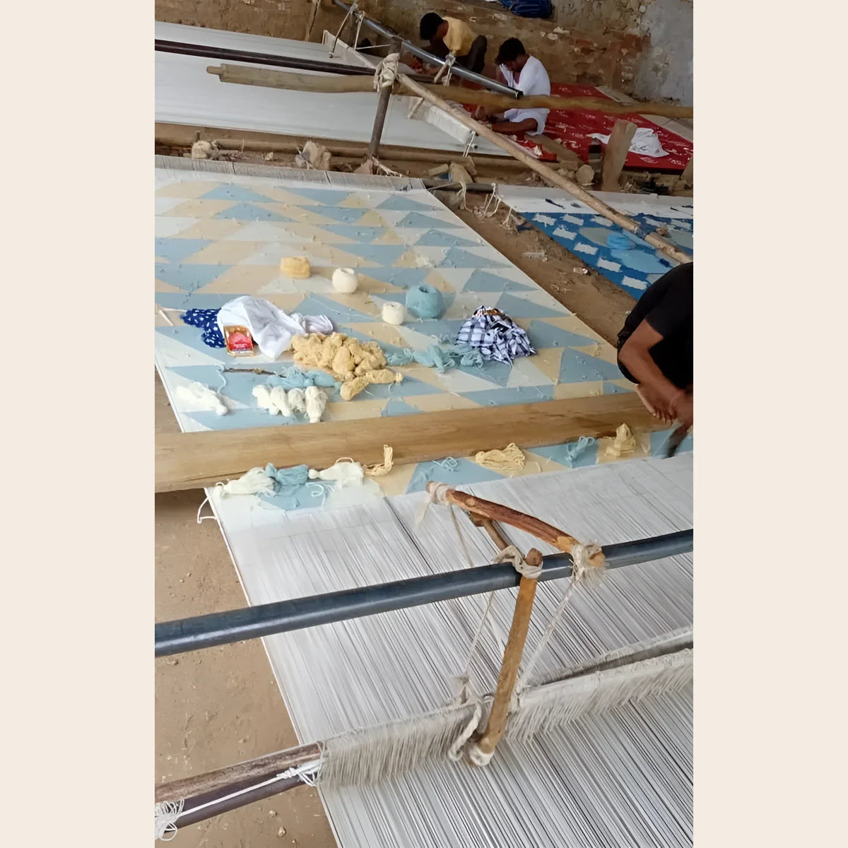 Artisans hand-weaving a Bespoke Flatweave Cotton Rug in blue and cream triangle pattern on a traditional floor loom.