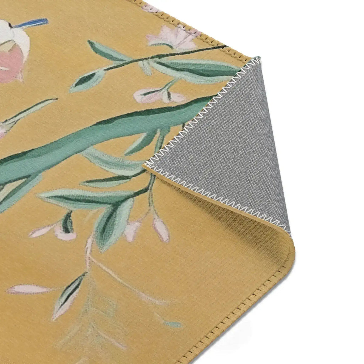 Close-up corner fold of Birds and Blossoms Accent Rug showing grey non-slip backing and stitched hem with partial floral pattern