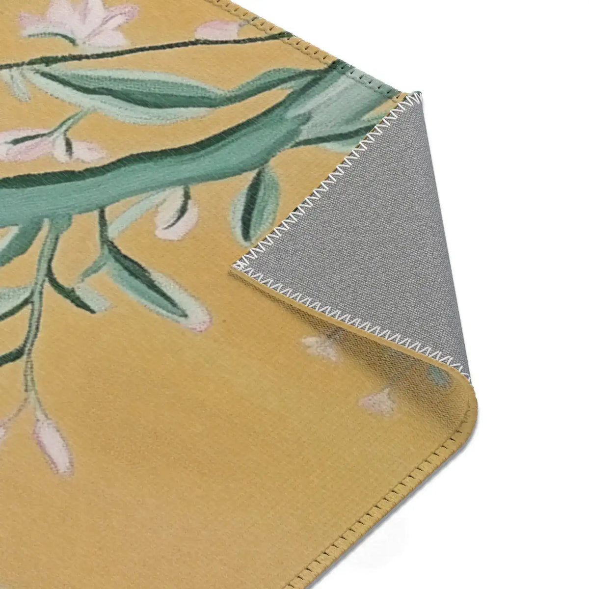 Corner fold of Birds and Blossoms Accent Rug exposing grey backing and overlock stitched edge with golden floral print face