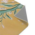 Corner fold of Birds and Blossoms Accent Rug exposing grey backing and overlock stitched edge with golden floral print face