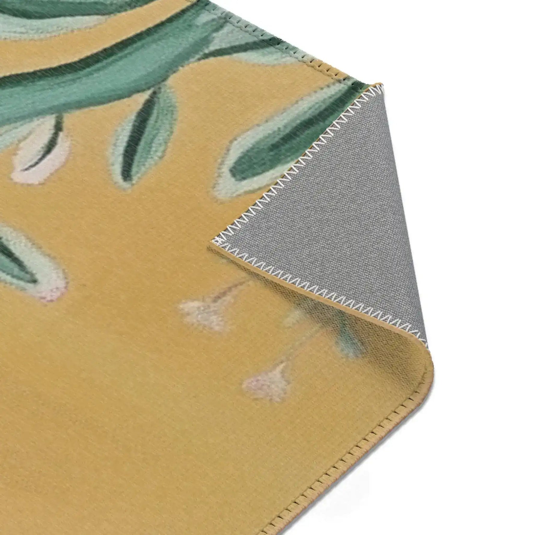 Diagonal corner fold of Birds and Blossoms Accent Rug revealing grey non-slip backing with overlock hem and green floral stitching