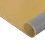 Rolled corner of Birds and Blossoms Accent Rug showing plain golden ochre woven face and grey non-slip fabric backing