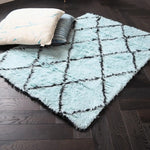 A stylish shag wool area rug featuring a black and blue diamond pattern, adding a touch of elegance to a living room setting. The plush texture of this living room area rug complements the dark wooden floor, while two decorative pillows rest on top, highlighting its cozy appeal. Perfect for those seeking quality rugs for living room spaces.