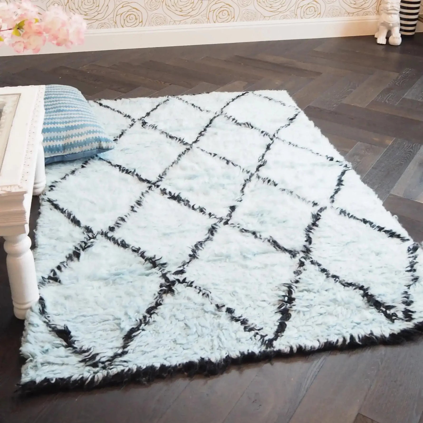 A cozy Black and Blue Diamonds Shag Wool Rug is elegantly placed in a stylish living room. This area rug, perfect for living room spaces, features a plush texture and a modern design with intersecting black lines on a soft blue background. Ideal for those seeking luxurious wool rugs for their living room decor.
