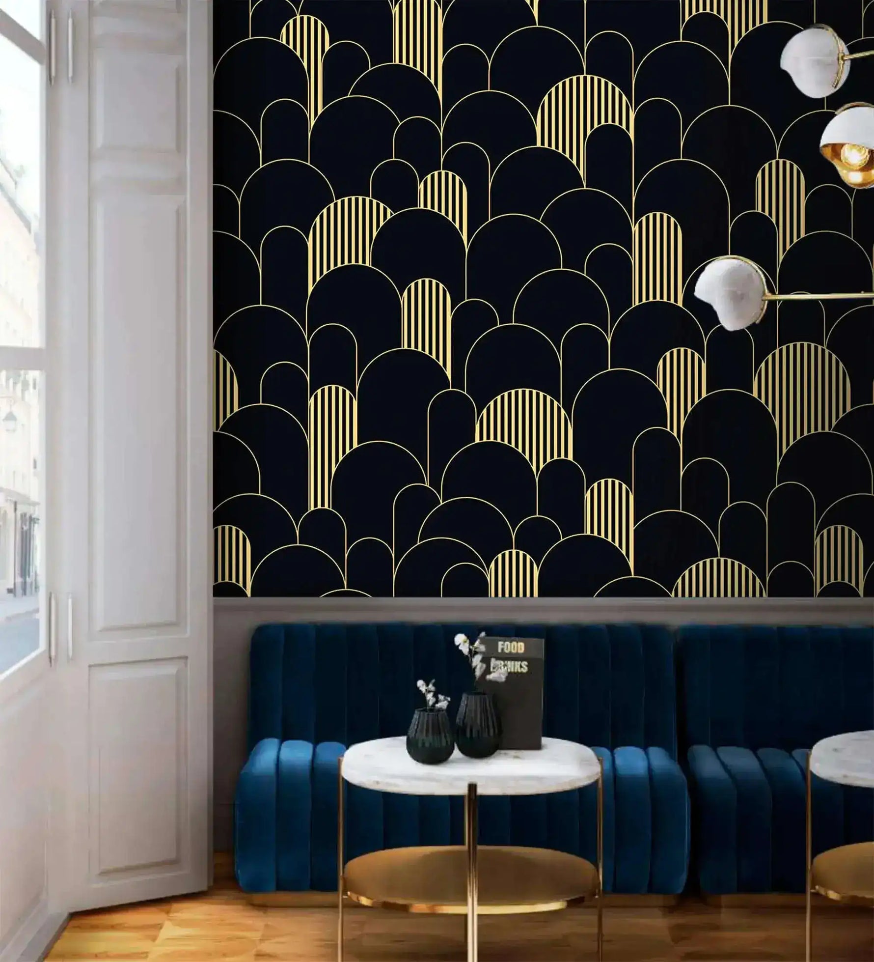 Black and gold art deco arch wallpaper above a blue velvet banquette with marble bistro tables