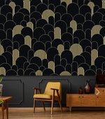 Black and gold art deco arch wallpaper above dark wainscoting with mustard chair and wood credenza