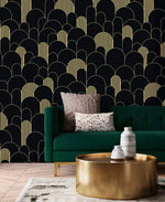 Black and gold art deco arch wallpaper behind an emerald velvet sofa with brass drum coffee table