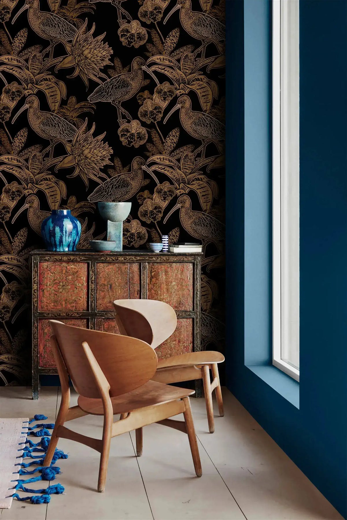 Black and gold bird wallpaper in corner with carved wood cabinet, blue vases and curved wood chair