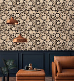 Black and gold damask floral scroll wallpaper above navy panelling with copper lamps and tan leather