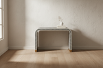 Black and white stripe waterfall bone inlay console table with brass feet against a plaster wall.