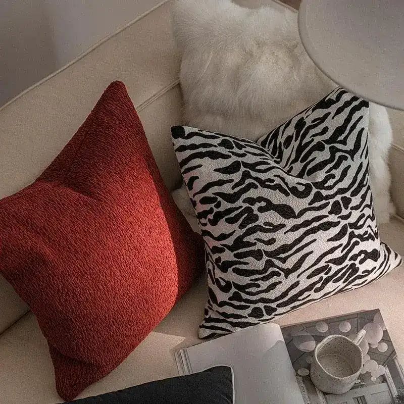 Black and white zebra print throw pillow cover with fringes, styled on a cozy couch alongside a textured red pillow.