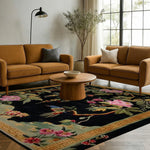 Black Floral Symphony hand-tufted rug under caramel sofas — black field with pink tropical blooms and bird motif, gold key border