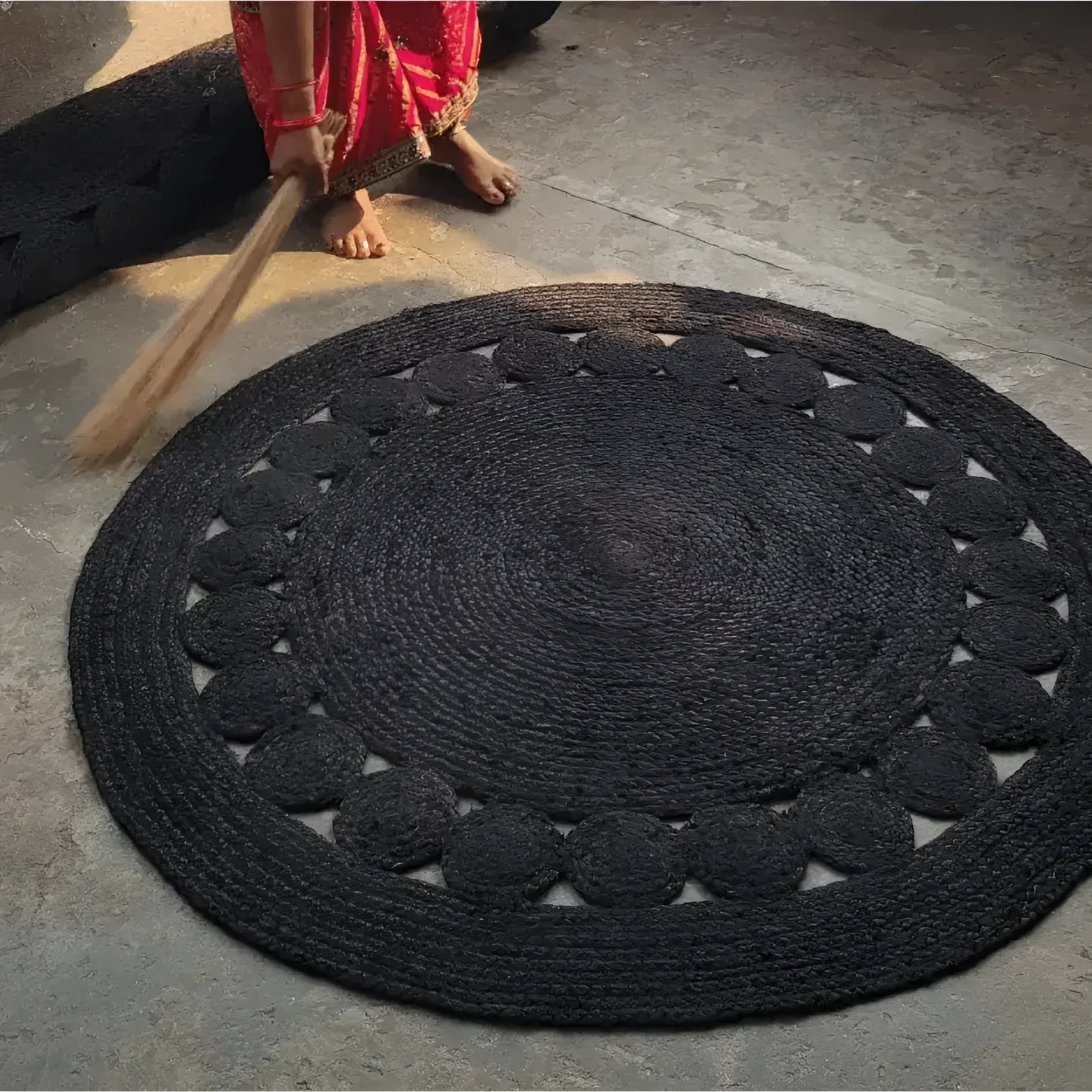 A beautifully handcrafted black round jute rug placed on a stone floor, perfect for enhancing your office or living room. This large area rug features an intricate woven design, adding a touch of elegance and natural texture to any space.