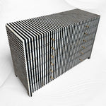 A modern six-drawer dresser with a bold black and white vertical striped pattern and small gold drawer pulls, shown on a white wavy background.