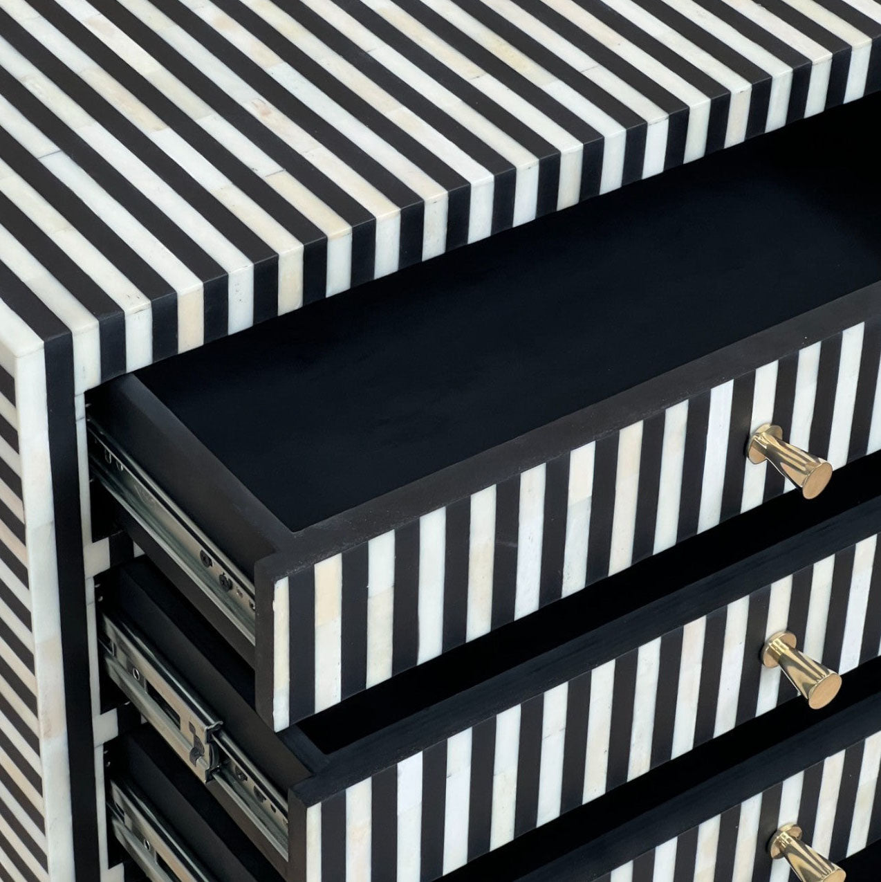 Close-up of a black and white striped furniture piece with an open drawer showing a black interior and gold-toned hardware.