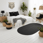 Modern bedroom with a black oval rug, white bed, and decorative plants.