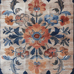 A beautifully detailed Blossom Artistry Hand Knotted Area Rug featuring an intricate floral design in vibrant shades of blue, orange, and beige. This square rug, reminiscent of classic Persian rugs, is perfect for adding a touch of elegance to a living room. Made from high-quality wool, this large living room rug offers both durability and style.