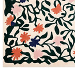 This vibrant area rug features a hand-tufted design with colorful blossoms and intricate green vines on a light backdrop, creating a lively and artistic pattern.