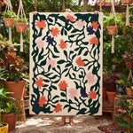Person holding a floral patterned rug in a garden setting with plants and macramé hangings.