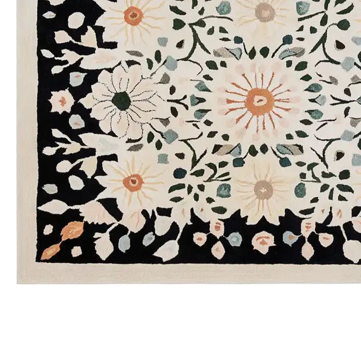 This Blossom Radiance Hand Tufted Wool Rug features a vibrant floral design with intricate blooms in soft hues of green, orange, and beige, set against a bold black background. The area rug adds a touch of elegance and warmth to any room.