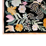 A detailed view of the Blossom Safari Hand Tufted Wool Rug, featuring a vibrant floral design with pink, orange, and white flowers against a dark backdrop. This area rug showcases intricate patterns and a soft texture, perfect for adding a touch of elegance to any room.