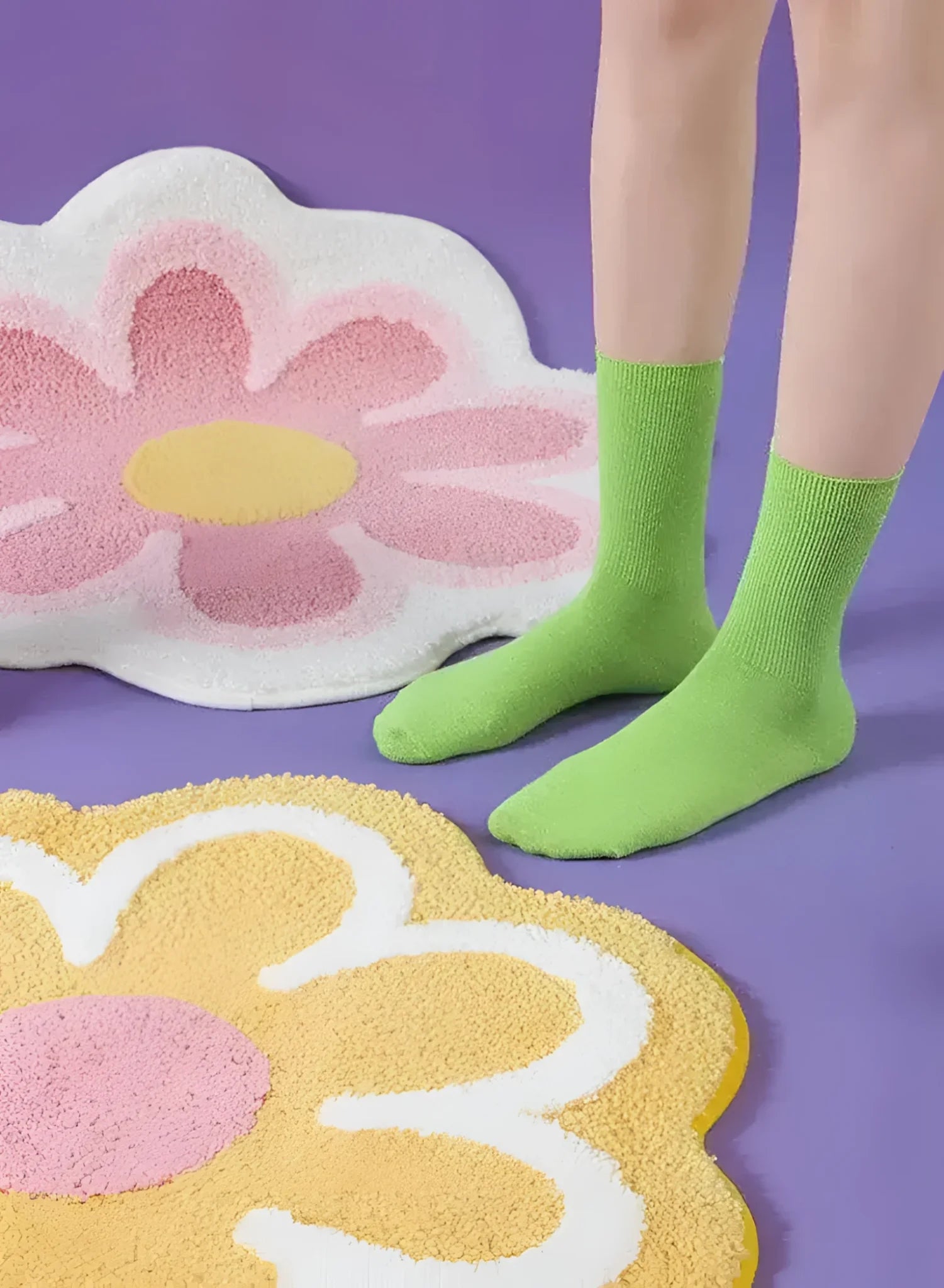 A vibrant image featuring two flower-shaped area rugs on a purple floor. One rug displays a bright yellow and white flower design, while the other showcases a pink and white motif. A person wearing green socks is standing next to the rugs, adding a playful touch to the scene.
