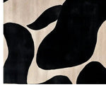 A stylish area rug featuring an abstract black and cream pattern. The design consists of large, organic shapes that create a modern and artistic look, perfect for adding a touch of elegance to any room.