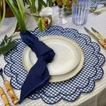 Close-up blue and white gingham scalloped placemat with navy border, stacked white plates, bamboo cutlery