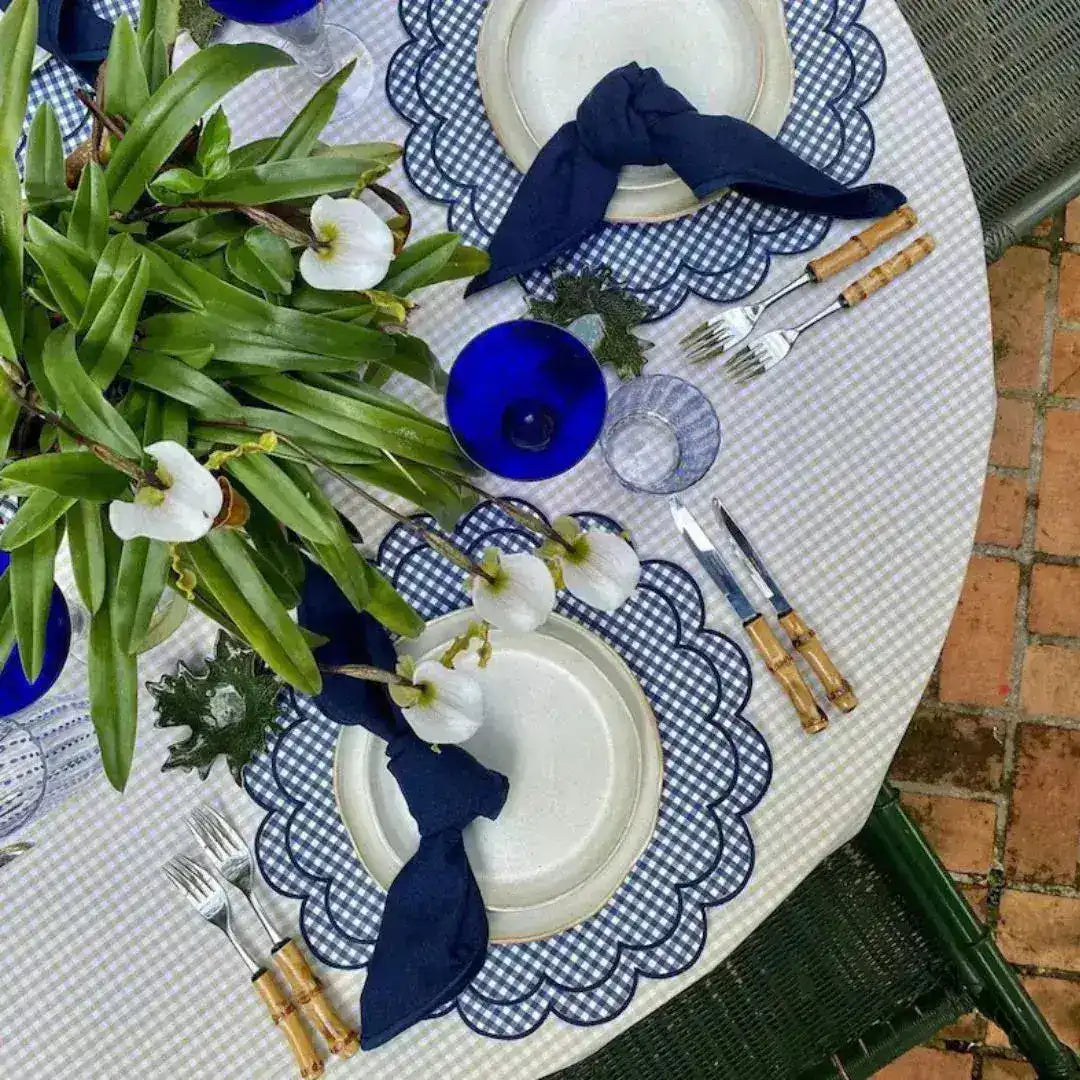 Overhead table with blue and white gingham scalloped placemats, navy napkins, bamboo cutlery, white orchids