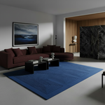 A modern living room featuring a large blue geometric area rug, a dark red sectional sofa, black coffee tables, and a framed dramatic landscape print on the wall.