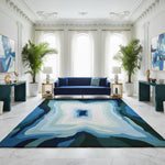 Modern living room with a blue sofa, patterned rug, and decorative plants.