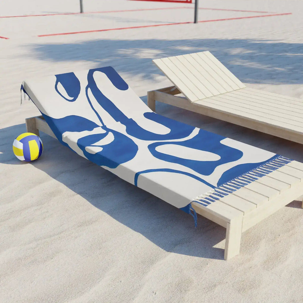 Blue flow abstract beach towel draped on wooden sun lounger on sandy beach beside a yellow volleyball