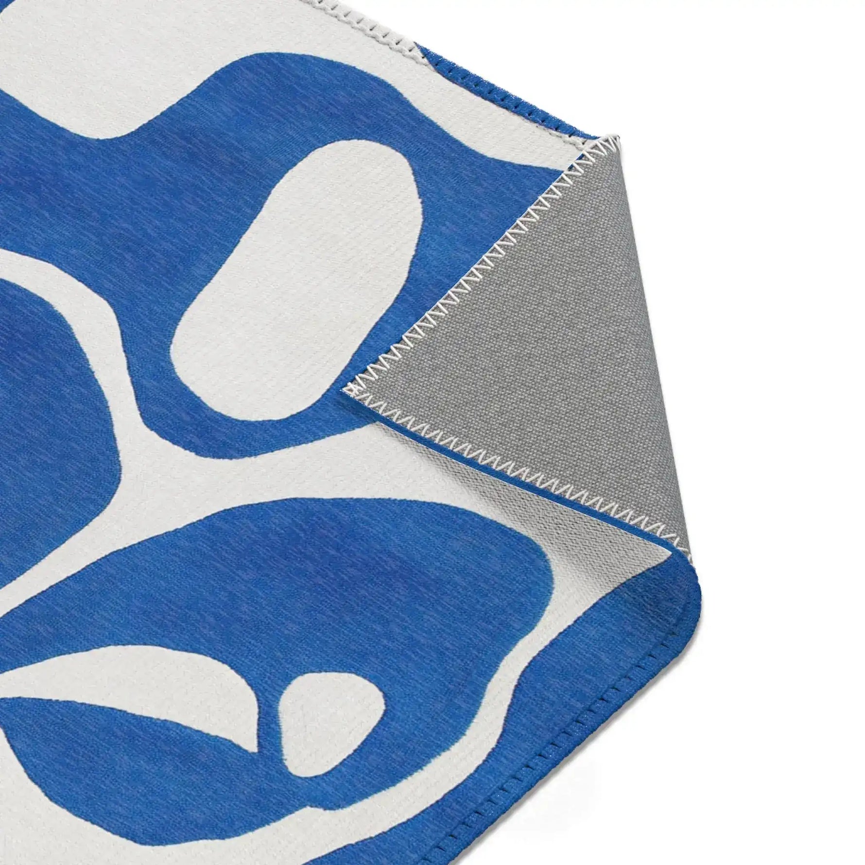 Corner fold detail of blue flow abstract modern rug showing gray backing and serged seam edge