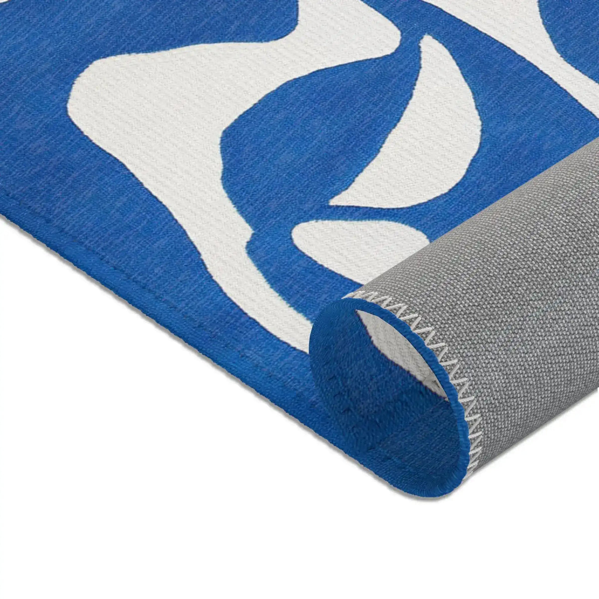 Close-up rolled corner of blue flow abstract modern rug revealing gray backing fabric and serged edge