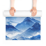 Hands unrolling the blue watercolor mountain yoga mat over its painted peaks