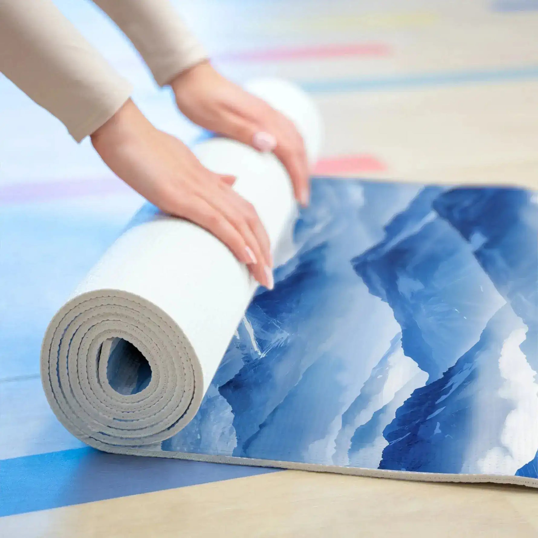 Hands rolling up the blue mountain yoga mat on a light wood floor